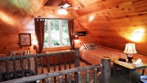 Ein gemütliches Blockhauskabinenzimmer mit Holzvertäfelung, einem Bett mit gemusterten Betttextilien, einem Nachttisch mit Lampe und einem Fenster mit Vorhängen.
