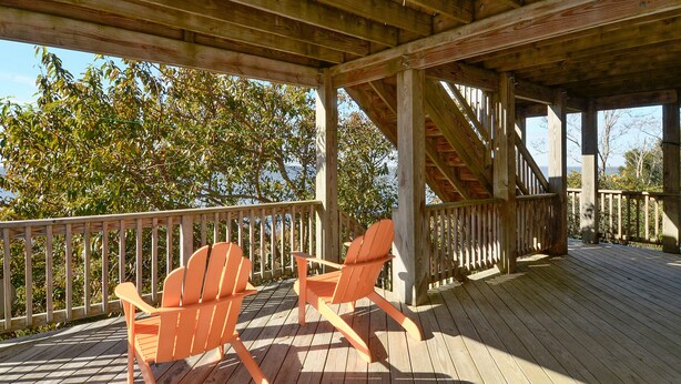 Une terrasse en bois avec deux chaises Adirondack et une rambarde en bois.