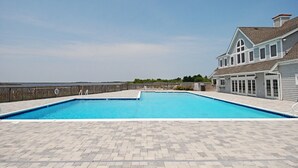 Une piscine avec une terrasse en bois, une grande maison dotée d’un toit à pignon et une vue sur l’océan.