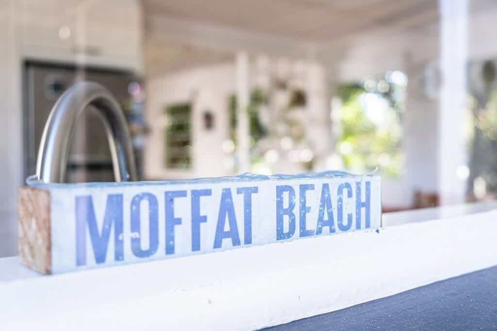 A sign with the text "MOFFAT BEACH" on a white surface.