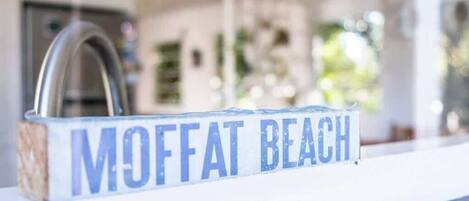 A sign with the text "MOFFAT BEACH" on a white surface.