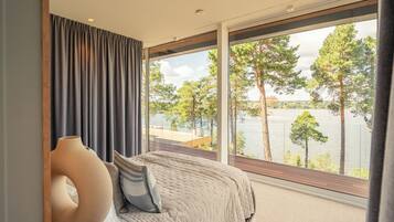 A bedroom with a large window overlooking a lake and trees.