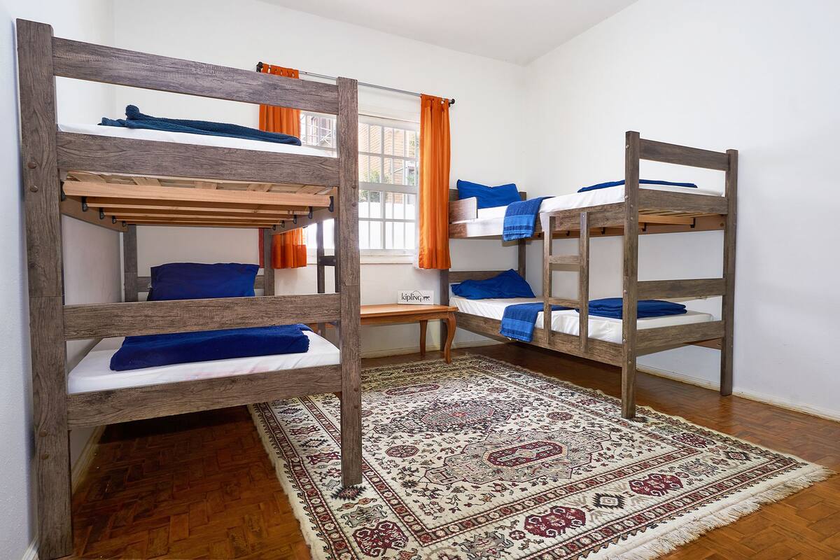 A dormitory room with three bunk beds, a wooden bench, and a patterned rug.