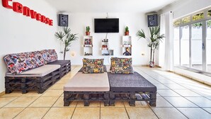 Una sala de estar con un sofá y un banco hechos de palés de madera, un televisor de pantalla plana montado en la pared y plantas en macetas.