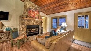 A cozy living room with a stone fireplace, wooden ceiling, and a comfortable leather sofa. - Dog Friendly 10 Acre Retreat Fly Fishing and Pond (Mineral Bluff)