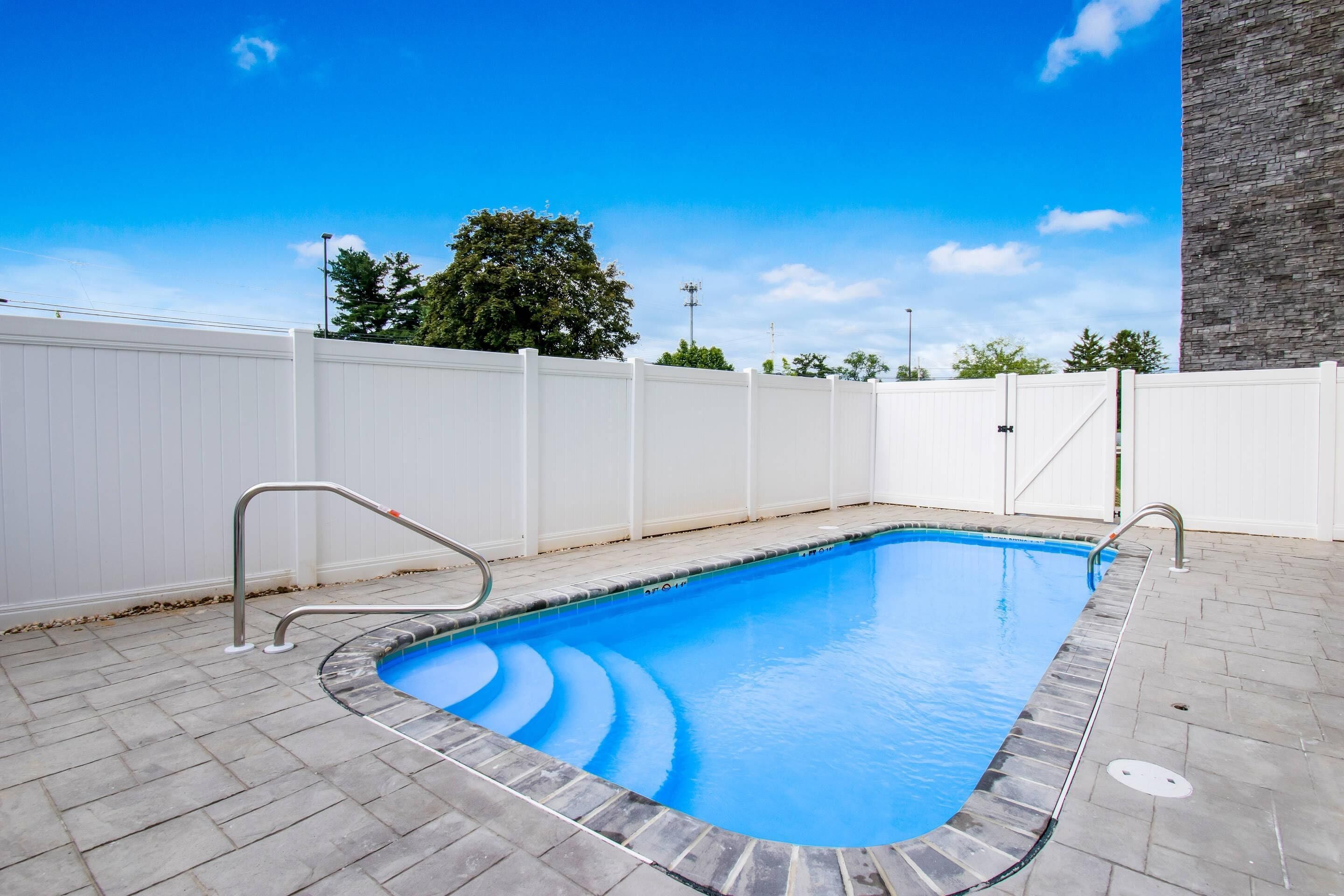 Piscina rectangular con revestimiento azul, rodeada por una cerca blanca y un muro de piedra en un lateral.