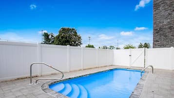 Piscina rectangular con revestimiento azul, rodeada por una cerca blanca y un muro de piedra en un lateral.