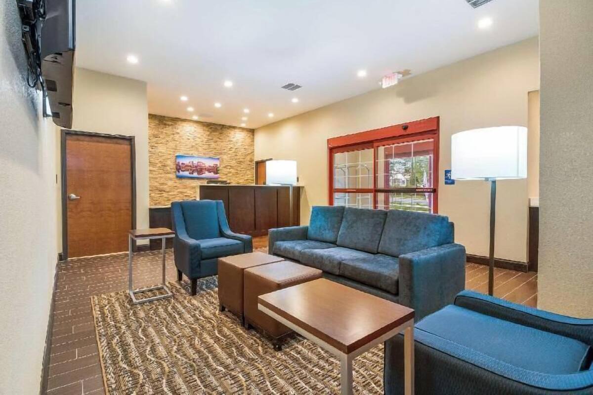 Un hall d’hôtel avec un mur décoratif en pierre, un canapé bleu, une petite table, un fauteuil bleu, un lampadaire et un téléviseur.