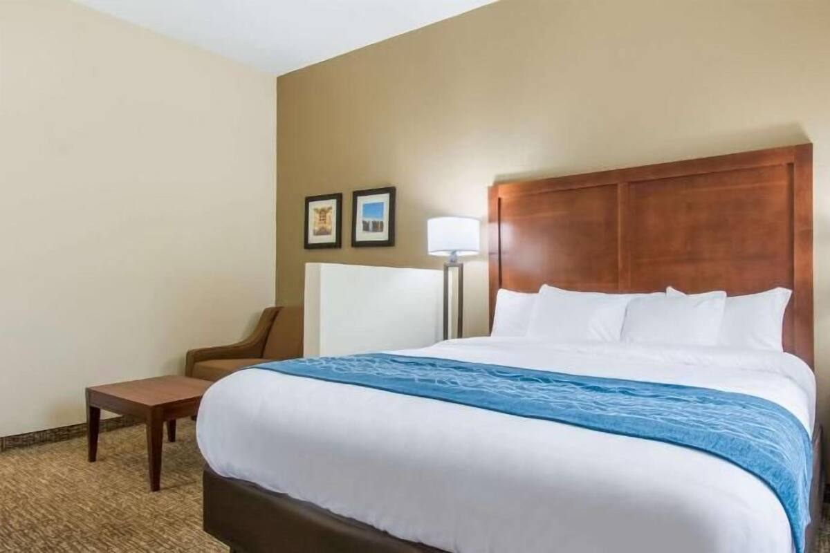Une chambre d’hôtel avec un grand lit, une chaise, une table de chevet et une lampe.
