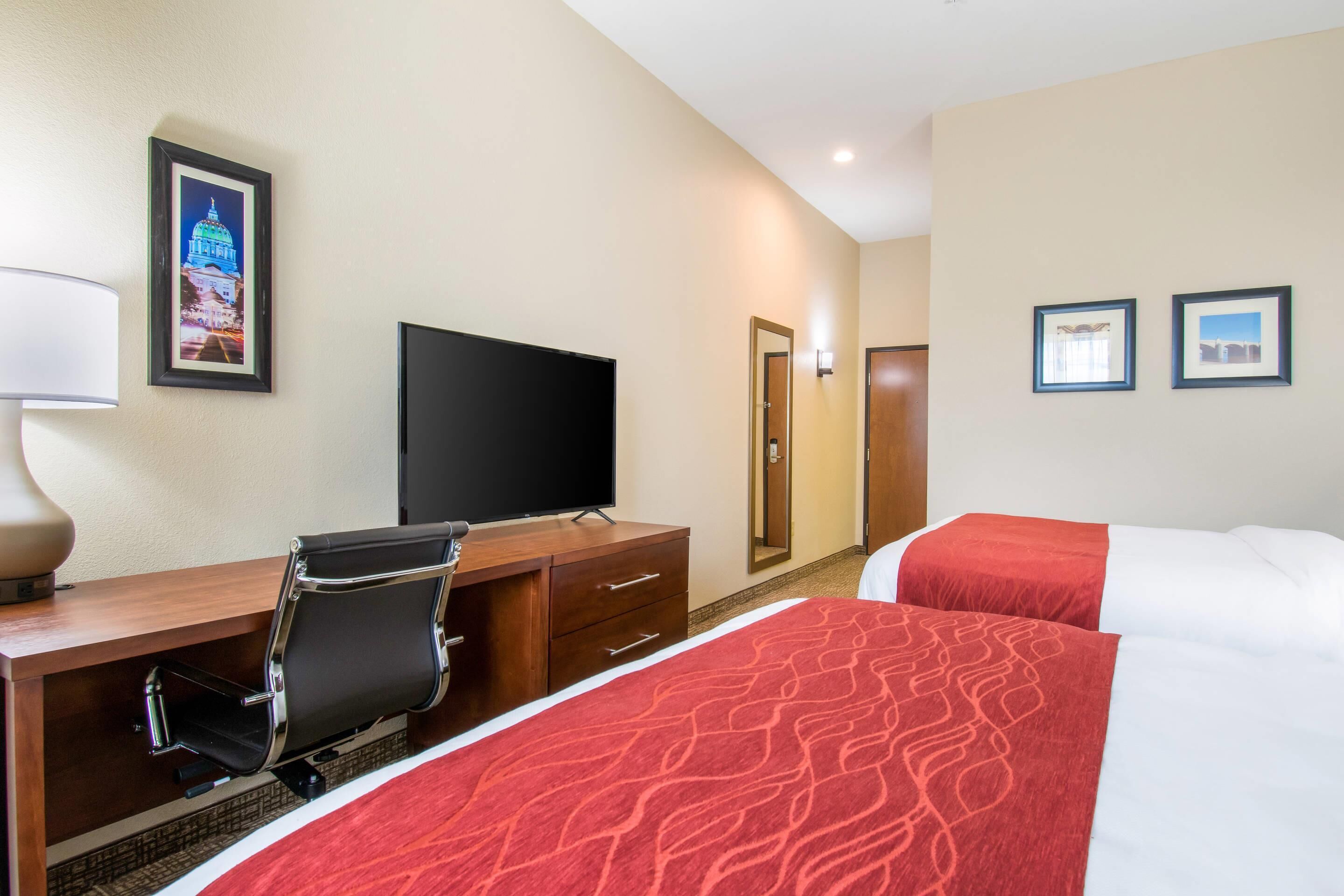 Une chambre d’hôtel avec un lit, un bureau et une chaise, une télévision et deux tableaux encadrés au mur.