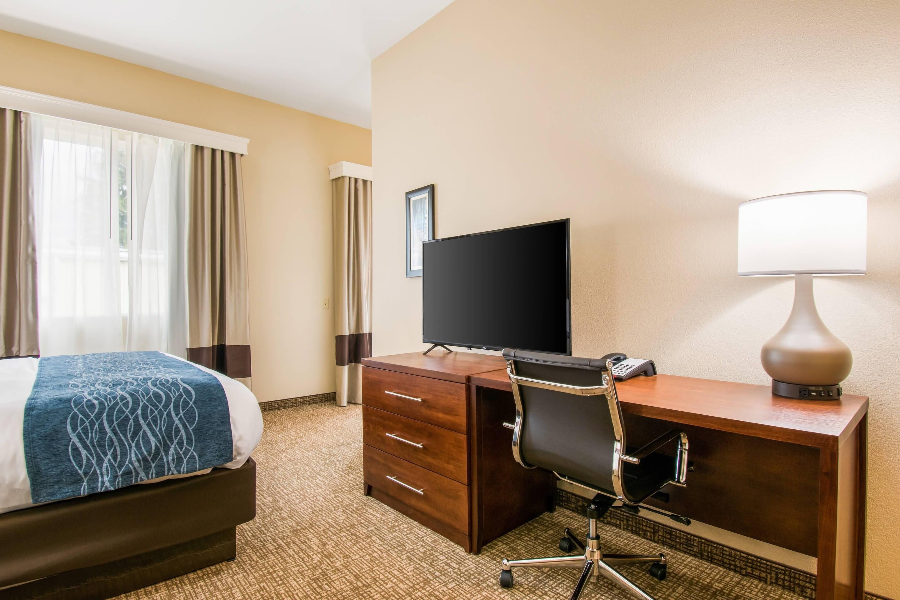 A hotel room with a bed, a desk with a computer, a lamp, and a television.