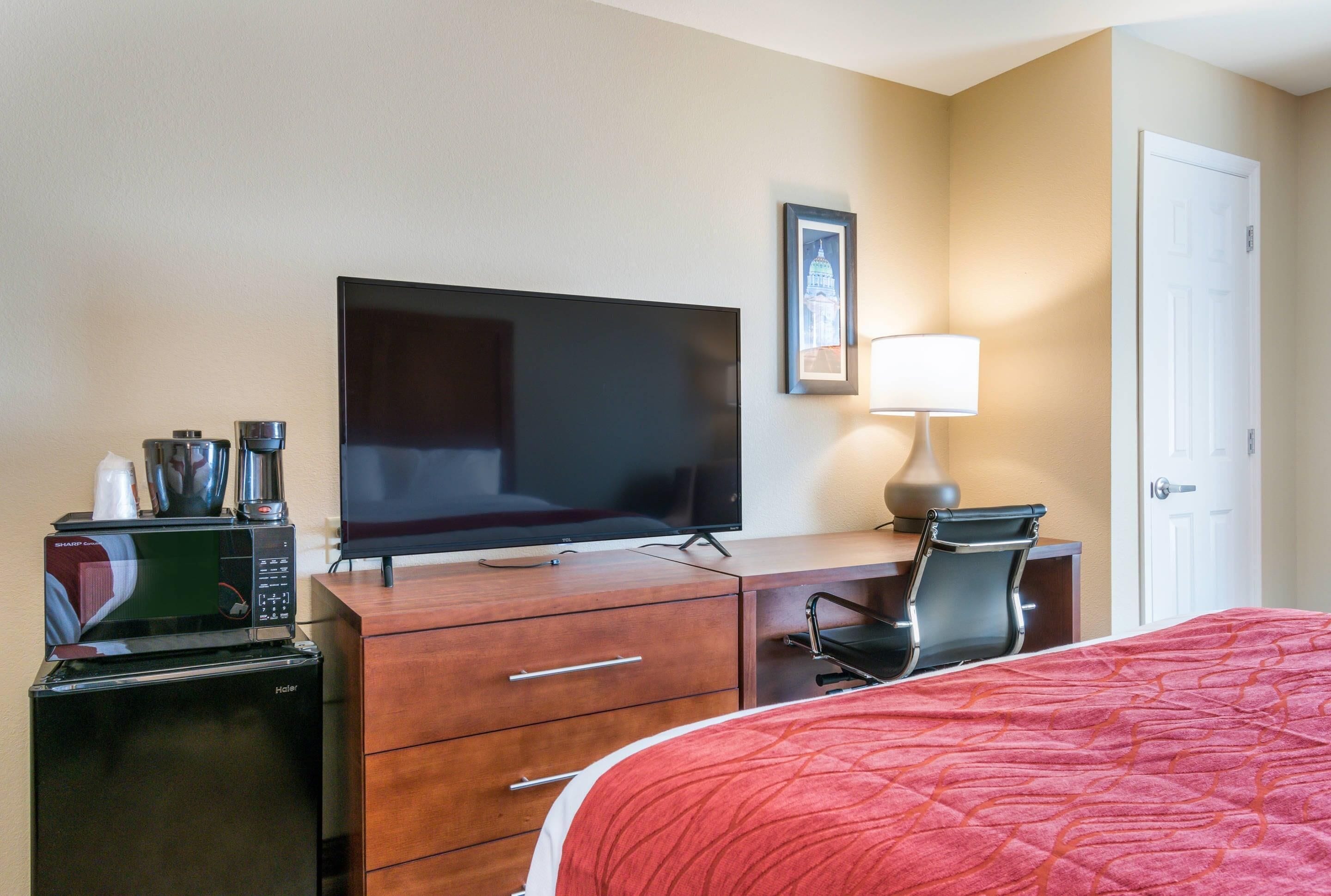 Una habitación de hotel con cama, televisión, escritorio con lámpara, silla y microondas.