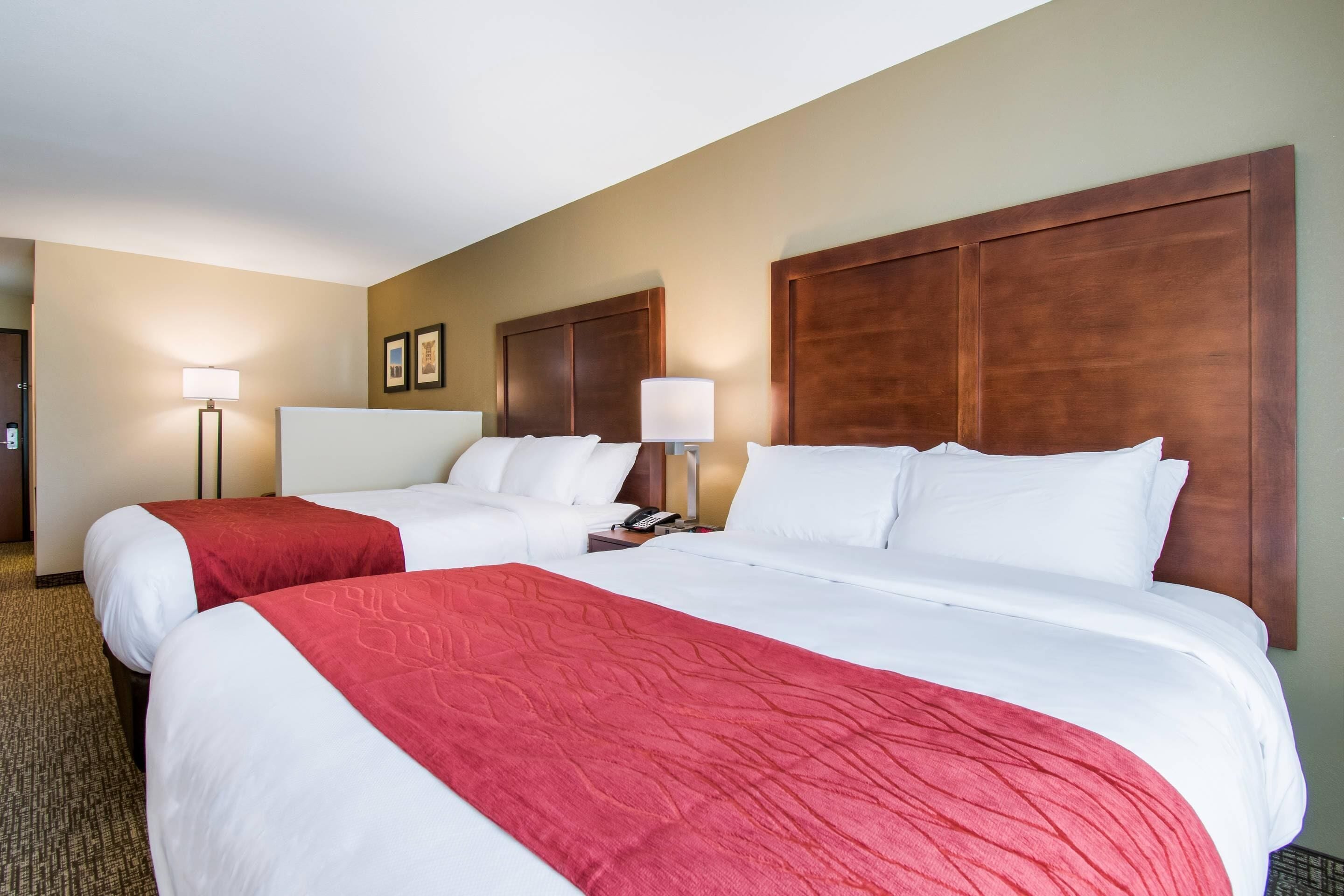 Une chambre d’hôtel avec deux lits, une tête de lit en bois, une table de chevet avec une lampe et un sol recouvert de moquette.