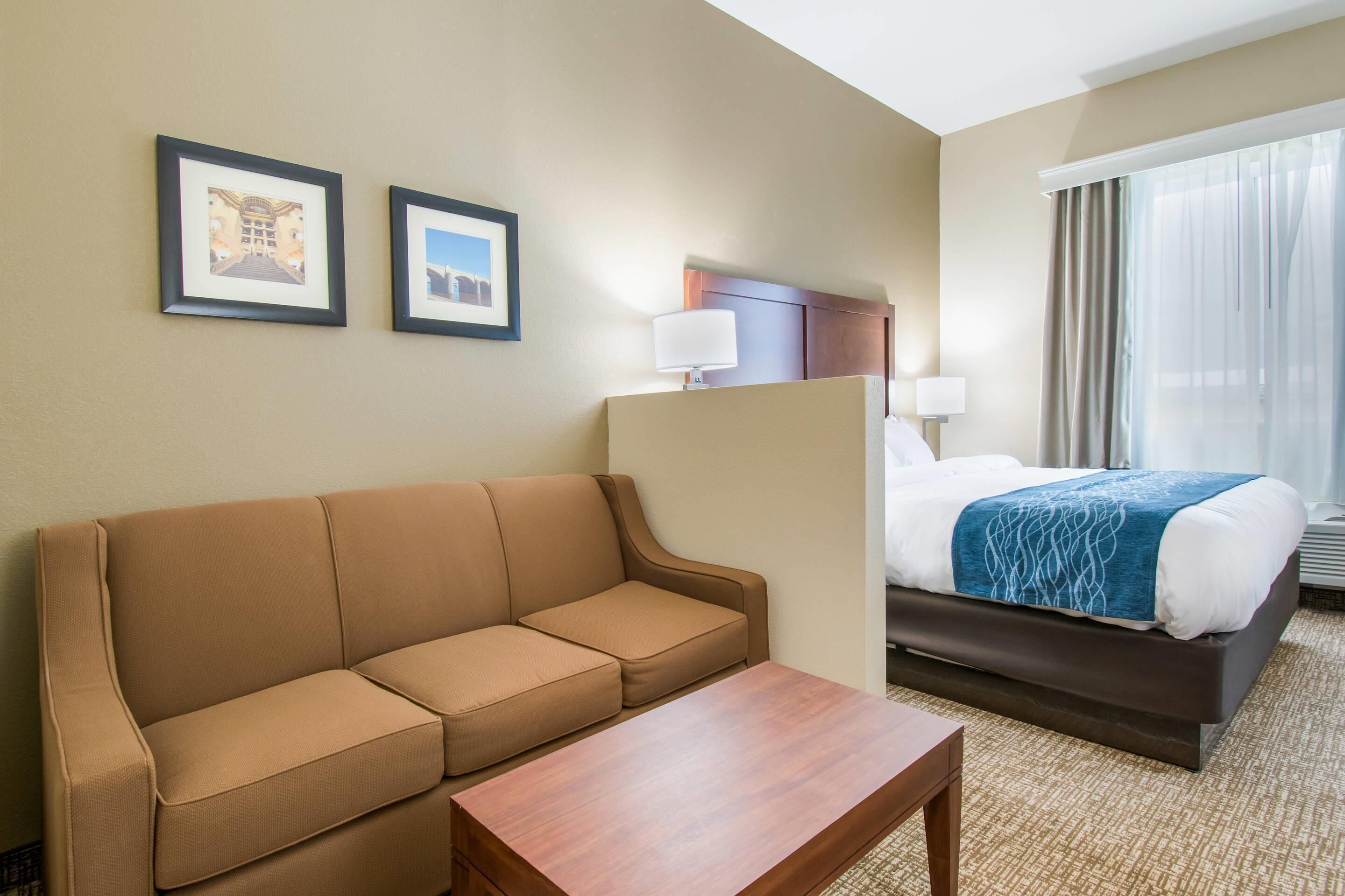 A hotel room with a sofa, a bed with a blue blanket, a nightstand, and two framed pictures on the wall.