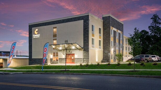 A hotel with a modern design, featuring a prominent 'Comfort Inn & Suites' sign, a covered entrance, and a parking area with several vehicles.