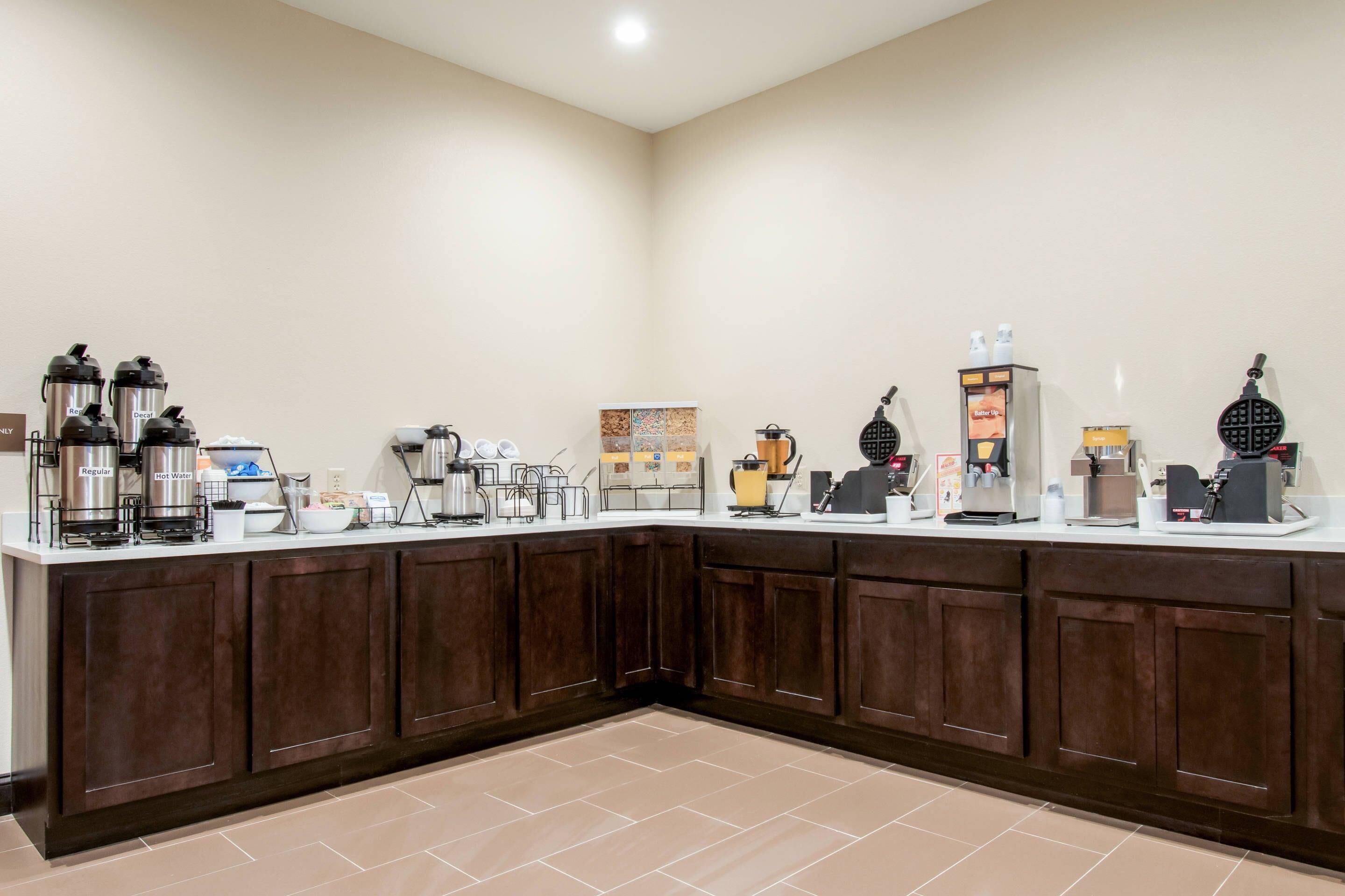 A hotel breakfast bar with coffee makers, a waffle maker, and a coffee station.