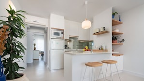 A modern kitchen with white cabinetry, a central island with stools, and a hanging light fixture. - Charming apartment on the beach with fantastic views in Puerto de Alcudia (Port d ´Alcudia)