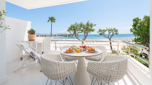 A balcony with a white table set for breakfast, overlooking a beach with palm trees and the sea. - Charming apartment on the beach with fantastic views in Puerto de Alcudia (Port d´Alcudia)