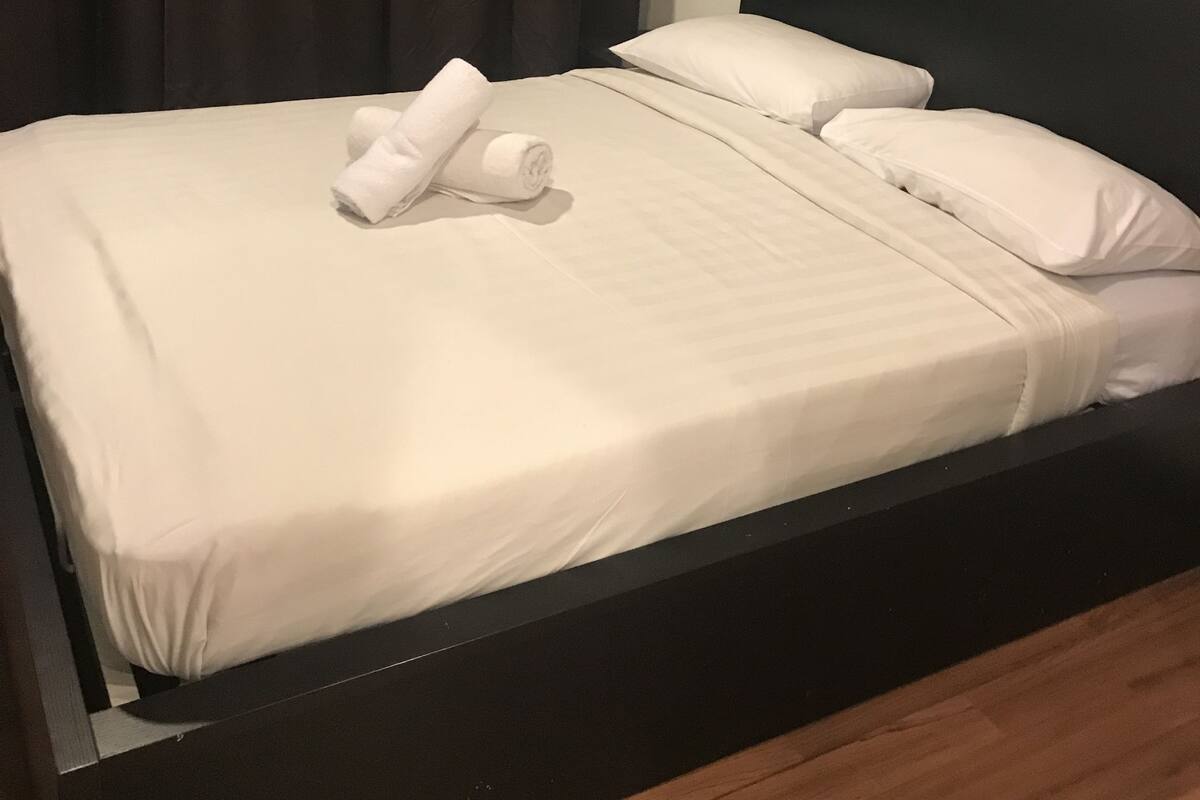 A neatly made bed with white linens and pillows, a dark headboard, and a wooden floor.