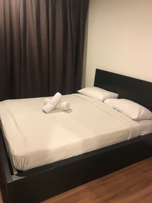 A neatly made bed with white linens and pillows, a dark headboard, and a wooden floor. - KL Taragon Apartment (Kuala Lumpur)