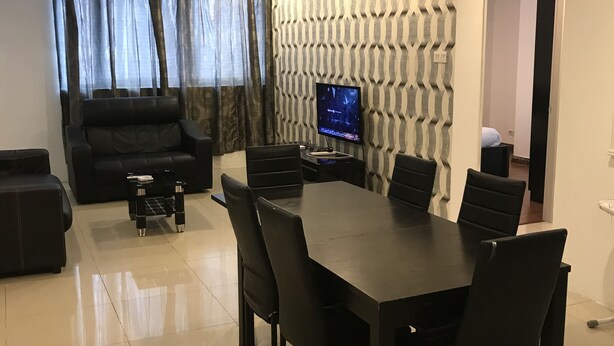 Un salon moderne avec un canapé en cuir foncé, une table à manger avec des chaises, un téléviseur à écran plat fixé à un mur orné de motifs et un ventilateur de plafond.