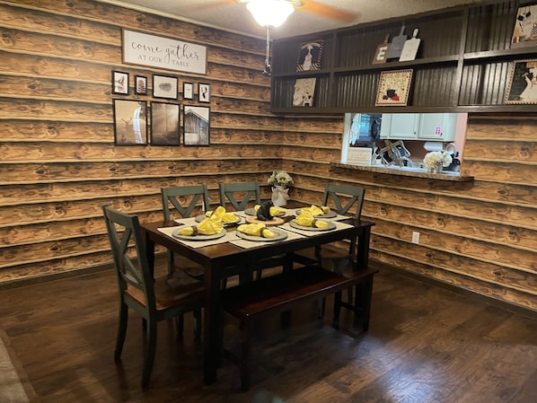 A dining area with a wooden wall, a table set with yellow napkins, and framed pictures on the wall.