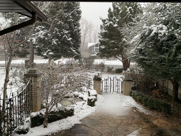 A snow-covered residential driveway with a gated entrance, stone pathway, and snow-laden trees.