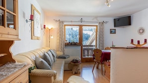 Una sala de estar acogedora con un sofá, una mesita, un armario de madera y vistas a un paisaje nevado a través de la ventana.