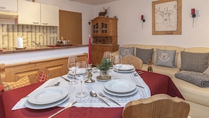 Un comedor con mantel rojo, platos blancos y cubiertos. Se observa un aparador de madera con puertas de cristal y una figurita de ciervo encima. También se ve un aparador de madera con puertas de cristal.