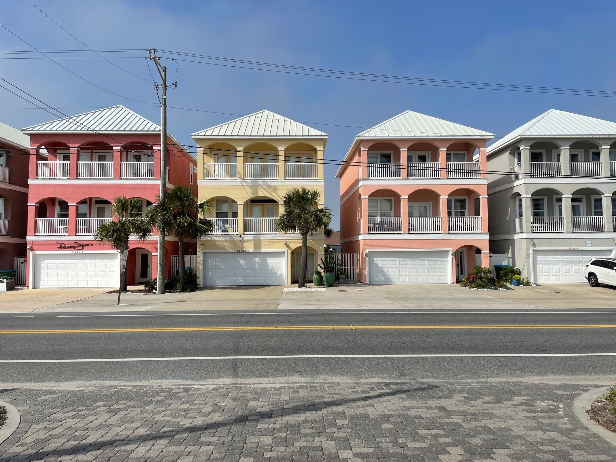 Una hilera de casas urbanas de tres pisos, con balcones, puertas de garaje y un cielo despejado.