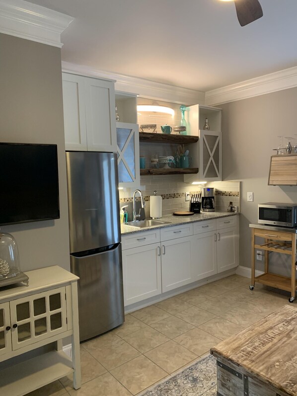 A modern kitchen with white cabinets, a stainless steel refrigerator, and a wooden countertop.