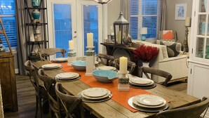 Un coin repas avec une table en bois dressée pour six personnes, entourée de chaises. Un lustre est suspendu au-dessus de la table, et des bougies y sont disposées.