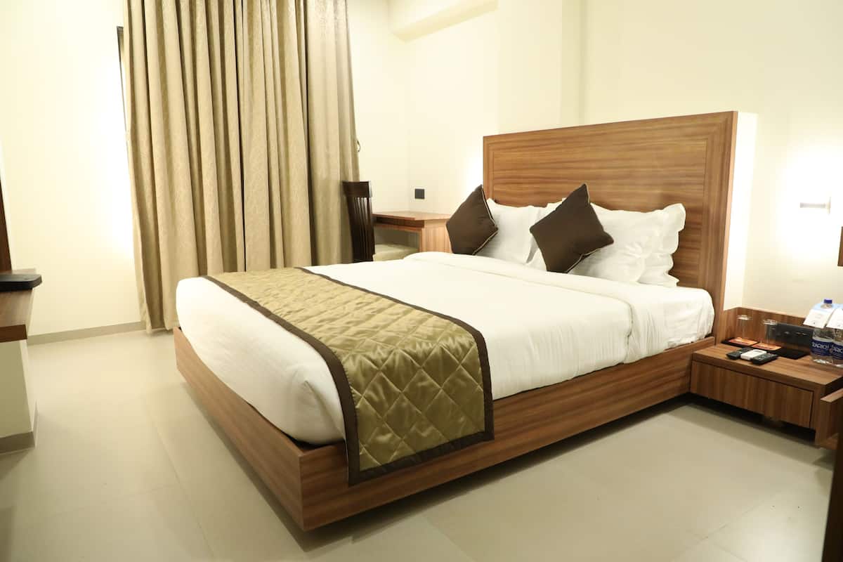 A hotel room with a large bed, wooden headboard, and a bedside table with a lamp and a bottle.