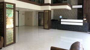 A modern hotel lobby with a reception desk, a glass elevator, and a decorative wall with a globe.
