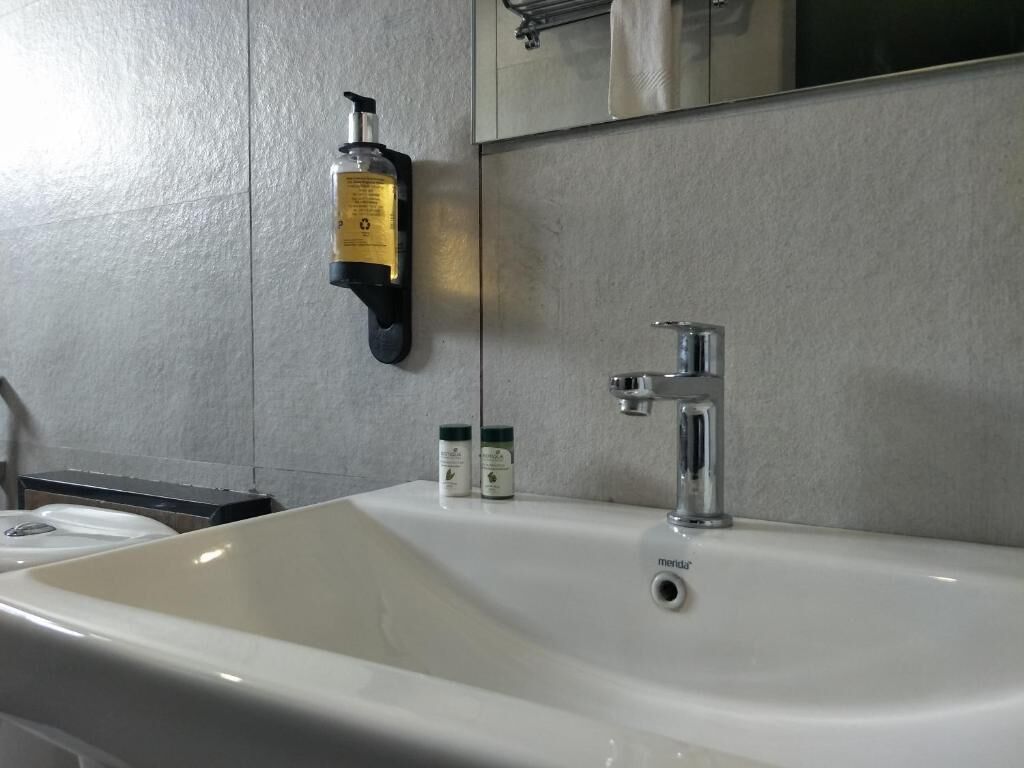 A bathroom with a white sink, a mirror, and a soap dispenser mounted on the wall.