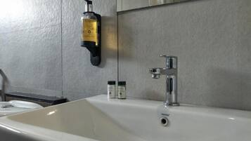 A bathroom with a white sink, a mirror, and a soap dispenser mounted on the wall.