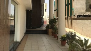 A covered walkway with tiled flooring, columns, and potted plants.