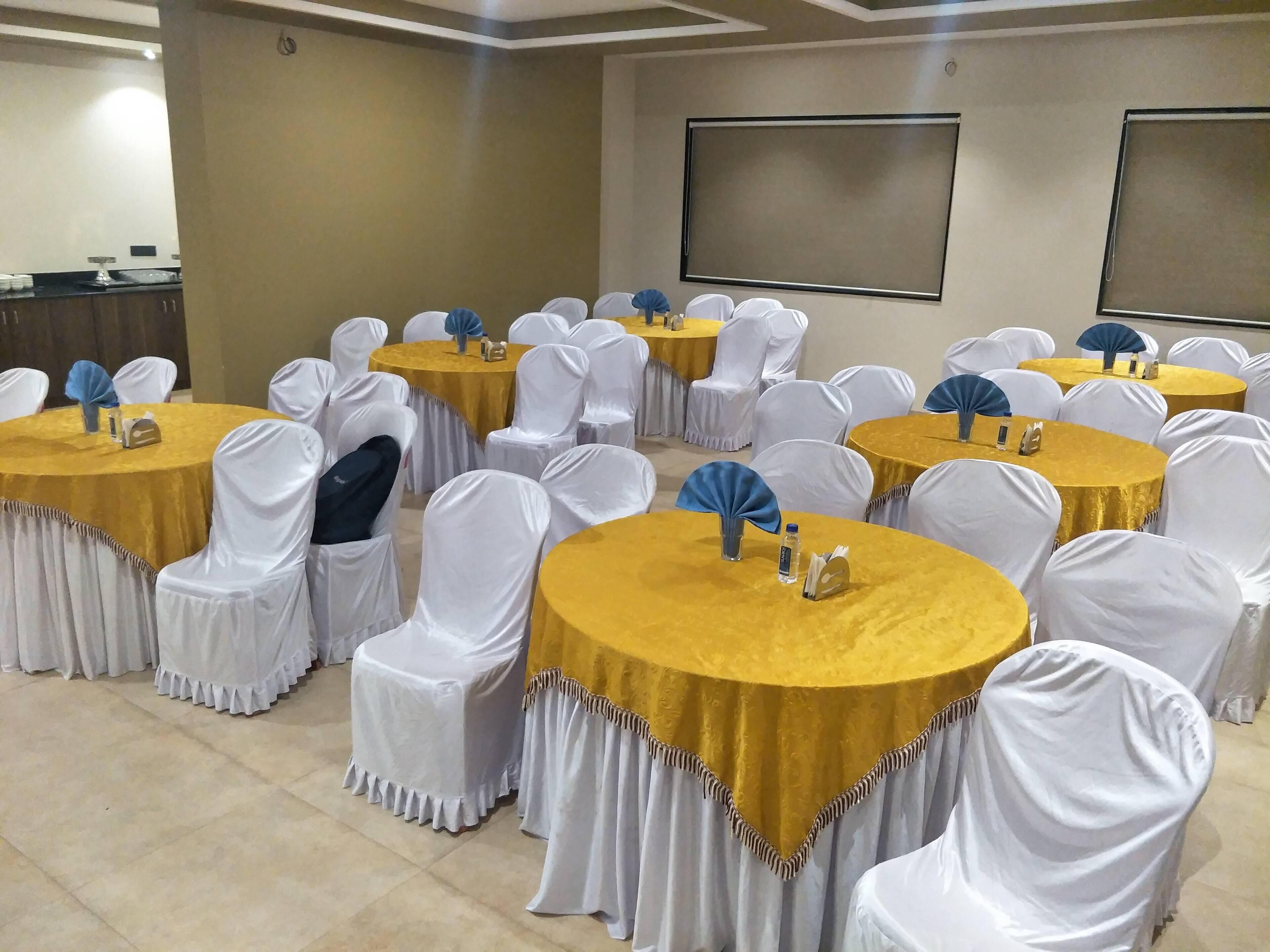 Una sala de conferències amb taules rodones cobertes amb camases daurades i cadires blanques amb petits ventiladors blaus.