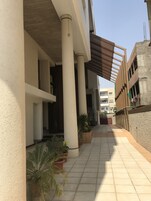 Un pasillo cubierto con columnas, plantas en macetas y piso de baldosas.