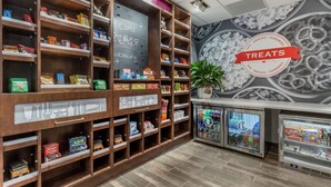 A snack and sundries section with shelves stocked with various packaged goods, a chalkboard with a welcoming message, and a wall mural. - Hampton Inn Camden (Camden)