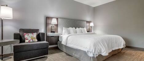 Una habitación de hotel con cama, una silla, una mesita de noche y una lámpara.