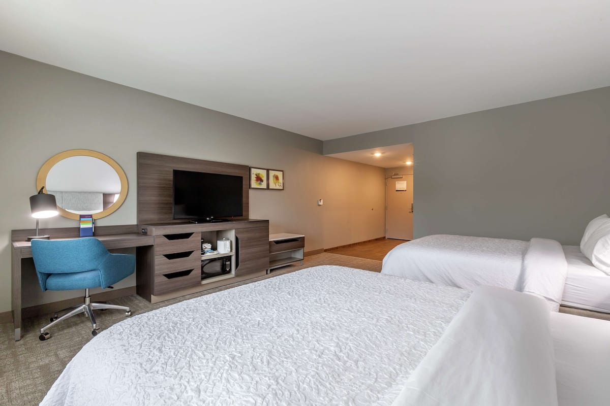 A hotel room with two beds, a desk with a computer, a TV, and a mirror.
