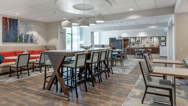 A spacious indoor area with a long dining table, multiple chairs, a sofa, and a kitchen area in the background. - Hampton Inn Camden (Camden)