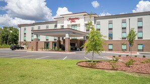 A Hampton Inn hotel with a modern facade, a covered entrance, and a landscaped front yard.