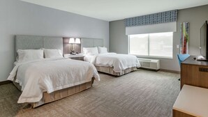 A hotel room with two beds, a desk, a chair, a lamp, a window with a view, and a radiator.