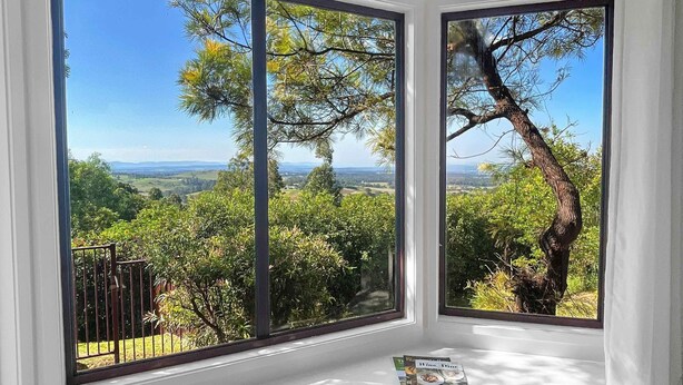 A room with large windows offering a view of a forest and distant hills.