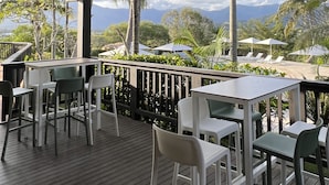 An outdoor patio with white tables and chairs, surrounded by palm trees and a view of mountains. - Rivland Resort (Paita)