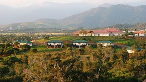 A residential area with houses on a hillside, surrounded by greenery and mountains in the background. - Rivland Resort (Paita)