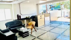 A modern reception area with a black leather sofa, a wooden chair, a small table, and a glass partition. - Namaha Stays (Hyderabad)