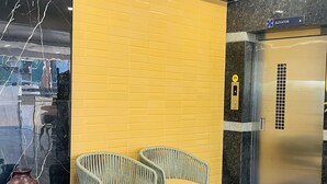 A hotel lobby with a check-in counter, two wicker chairs with cushions, a wall with a yellow panel, and an elevator. - Namaha Stays (Hyderabad)